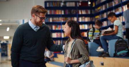 Male teacher and asian schoolgirl sharing high five standing in libraryの写真素材