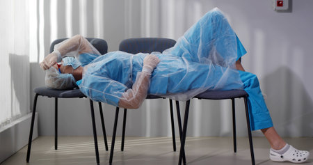 Tired doctor sleeping on row of chairs in hospital corridorの写真素材