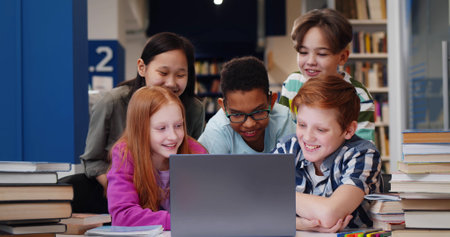 Happy multiethnic classmates using computer together in school libraryの写真素材