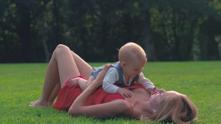 Young mother lying on green lawn together baby in summer dayの写真素材