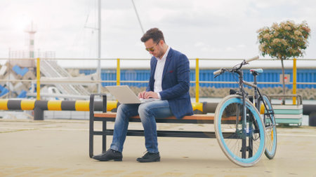 Man freelancer sitting on bench and working on laptop on embankmentの写真素材