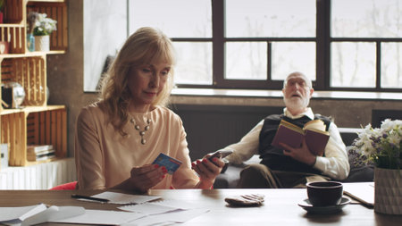 Portrait of senior woman with credit card and cellphone at homeの写真素材