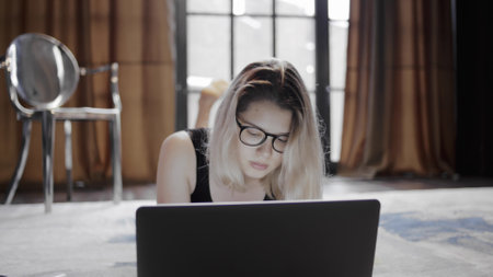 Young woman student lying on floor and typing on laptopの写真素材