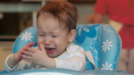 Baby boy sitting in baby chair and crying in kitchenの写真素材