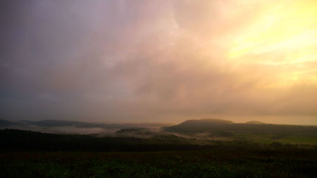 Summer sunset green hills and field with low cloudsの写真素材