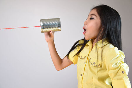 little girl using a can as telephone on a gray background.の写真素材