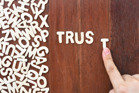 Word trust made with block wooden letters next to a pile of other letters over the wooden board...