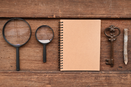 Blank notebook with pencil, key and magnifying glass on wooden backgroundの写真素材