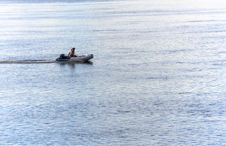 A girl alone in an inflatable boat with a motor floats on a blue river on a bright spring day