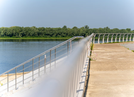 Tubular metal, curved, horizontal fence of the river embankment on a sunny day with a staircase. The foreground is blurred. COVID-19-free territoryの写真素材