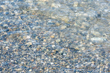 010_ Multi-colored sea pebbles on the shore, washed by a small wave of blue, blue, green color