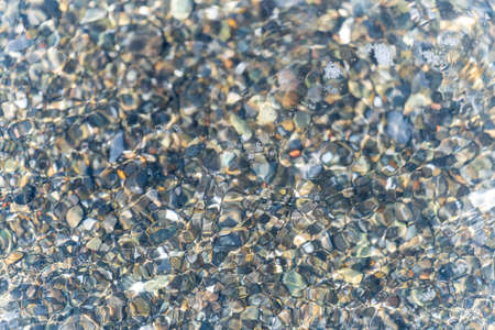 015_ Colorful sea pebbles on the shore, washed by a wave on a sunny summer day