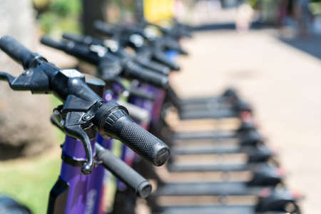 View of electric scooters standing in a row on the street on a sunny day. The foreground and background are blurred. Ecology, Transport of the futureの写真素材