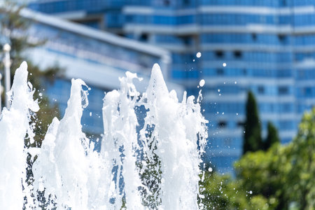 View of the foaming jets and splashes of the city fountain on a sunny day against the blurry background of residential buildings. Abstraction, backgroundの写真素材