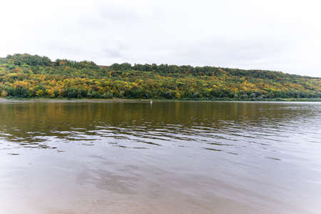 View of the river flowing along the hilly shore covered with forest in autumn
