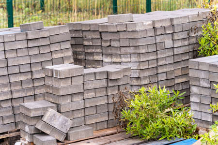 A stack of gray paving stones on a wooden pallet lies on the grass of the fenced territoryの写真素材