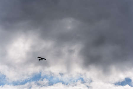A small private, light, single-engine plane in the dark sky, flying up to a thundercloud. View from the groundの写真素材