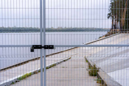 View of the metal lattice gate, closed with a padlock, on the river embankment, on an autumn cloudy dayの写真素材