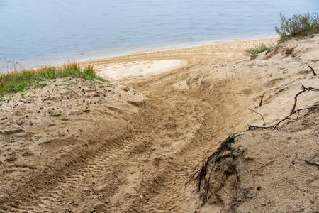 Car tire tracks on wet yellow sand, descending to the river on a rainy, cloudy autumn dayの写真素材