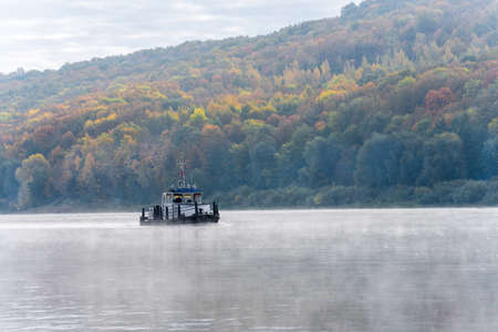 A beautiful view of a small towboat going down the river in the morning along a steep bank overgrown with forest. Autumn river landscapeの写真素材