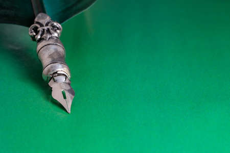 A view of the metal end of an antique goose feather lying on a table with a bright green background. Largeの写真素材