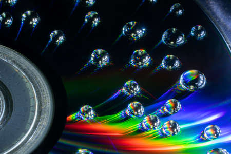 View of a CD fragment with water droplets and light refraction in them on a dark backgroundの写真素材