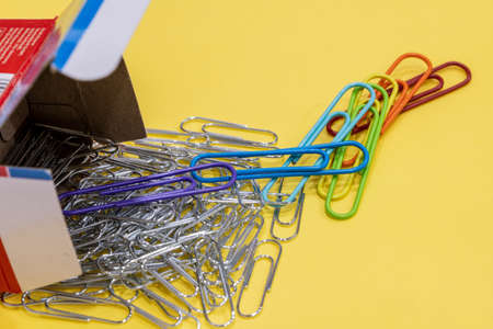 Top view of gray and colored metal paper clips, next to paper packaging on a yellow background. Large. Free space for copying, design or textの写真素材