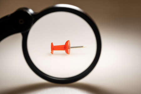 View of a red stationery button through a magnifying glass on a light background. Large. Free space for copying, design or textの写真素材