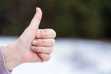 View of a woman's left hand, the thumb of which is raised up on the street. Hitchhiking sign. The background is blurredの写真素材