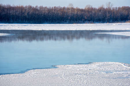 View of the river landscape on a sunny day, an ice-covered river in December. Reflection in the...