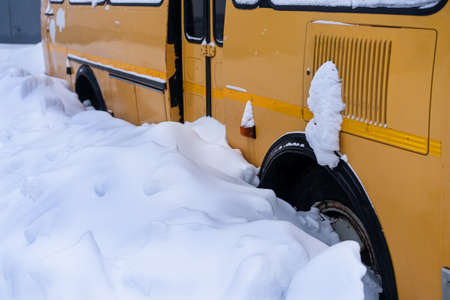 Side view of a fragment of a yellow vehicle covered with snow up to the top of the wheels. A fragment of a school bus stuck in the snowの写真素材
