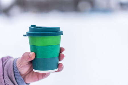 View of a paper cup of coffee in the hand on a winter day on a white background. The background is...