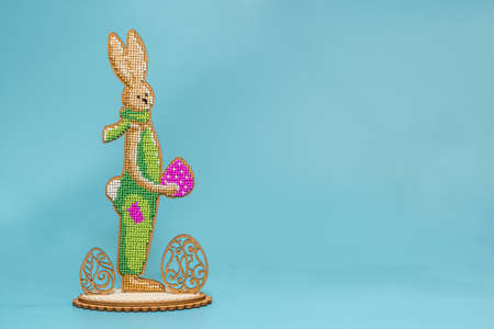 DIY, embroidery. View of the Easter bunny standing with an egg in his hands on a wooden stand. Place for the inscription. Turquoise backgroundの写真素材