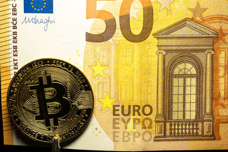 A view of the golden bitcoin cryptocurrency next to a fragment of a euro paper banknoteの写真素材