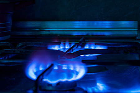 View of the gas burning with a blue flame in the burners of the kitchen gas stove on a dark...