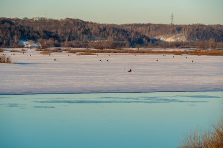 Beautiful spring morning river landscape with a part of the river covered with ice. Winter fishing on ice. A group of fishermen fishing in the distanceの写真素材