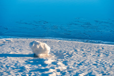 View of a snowball in the morning on an empty shore by a blue river covered with ice. The concept of...