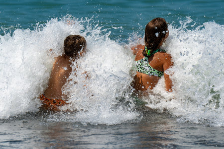 A view from the back of two children, a boy and a girl, diving into a splashing wave, on a summer,...
