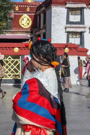 Local Tibetan woman pilgrim in Lhasa wearing traditional national Tibetan costume with beads in her hair on Barkhor squareの写真素材