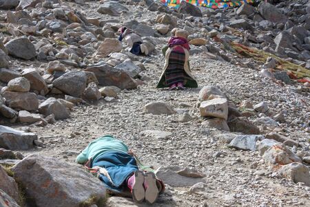Pilgrims prostrating on stony trekking kora around mountain Kailash pilgrimage route near Darchen, Tibet, Asiaの写真素材