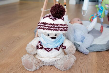 Teddy bear toy wearing a blue face mask and a baby boy lying in the backgroundの写真素材