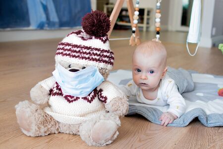 Teddy bear toy wearing a blue face mask and a baby boy lying in the background with his face visibleの写真素材
