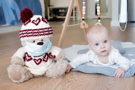 Teddy bear toy wearing a blue face mask and a baby boy lying in the background with his face looking to the rightの写真素材