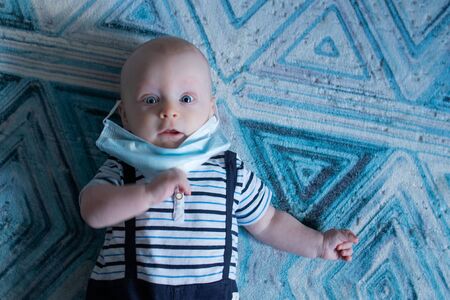 Baby boy lying on the blue geometric carpet and wearing a face maskの写真素材