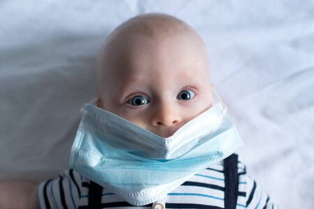 Baby boy lying on white cloth background and wearing a face mask portrait mouth coveredの写真素材