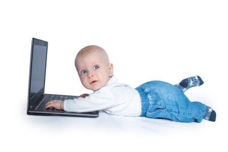 Baby boy lying on the floor with laptop looking in the upper right corner seriously with his foot upの写真素材