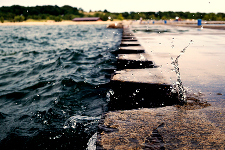 The splash of Wave on jetty pier with metal bollards. Water splashing during the Overcast weather. Splash froze over the pier. USA, state of Michigan, Michigan Lake.の写真素材