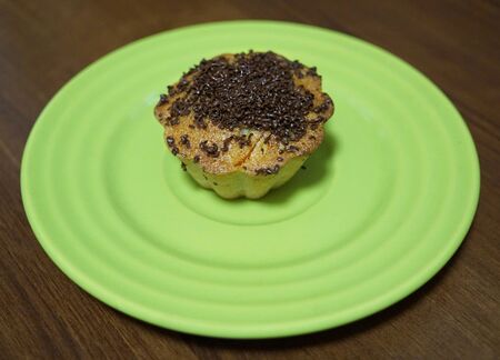 Vanilla Cupcake with chocolate chips on a mint color saucer. A plate stands on a wooden brown table