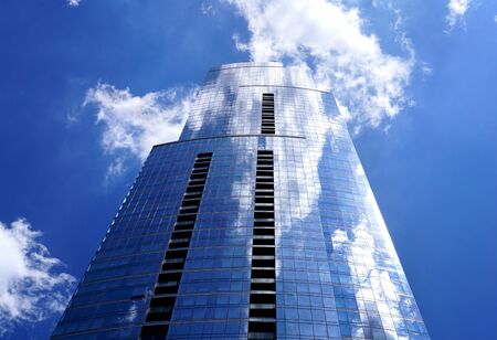 The building is from a low viewing angle close-up. White clouds are reflected in the window panes....