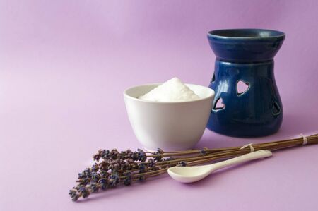 Lavander flowers, salty scrub in ceramic bowl, blue aroma oil lamp. Natural cosmetic composition on...